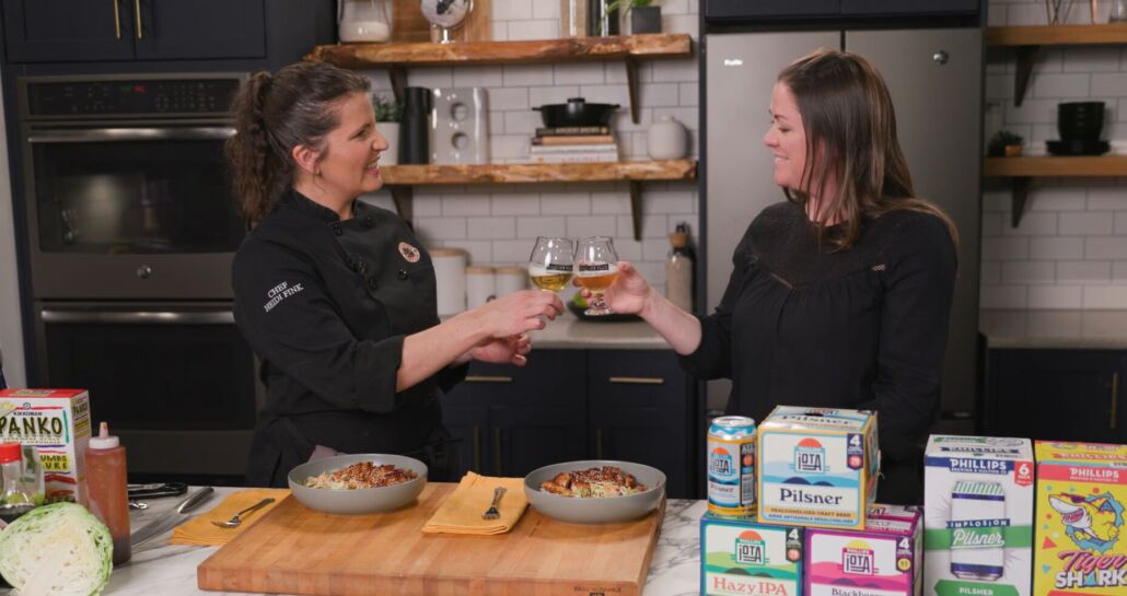 Chef Heidi and Shanyn Ward hold a glass of the Phillips Iota Pilsner in their hands.